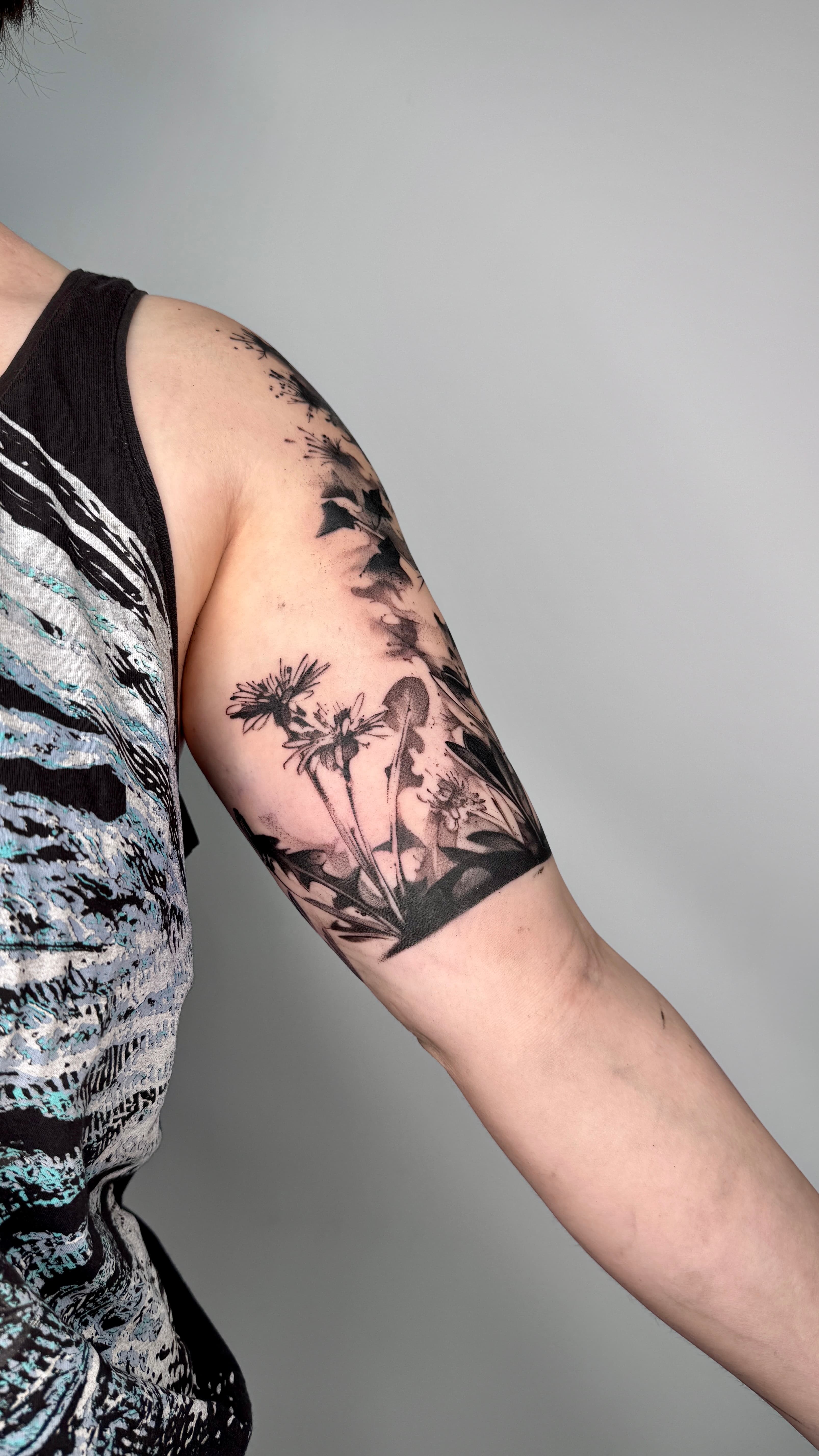 Detailreiches abstraktes Blumenwiese Tattoo am Oberarm und der Schulter, mit dunklen Schattierungen und floralen Elementen
