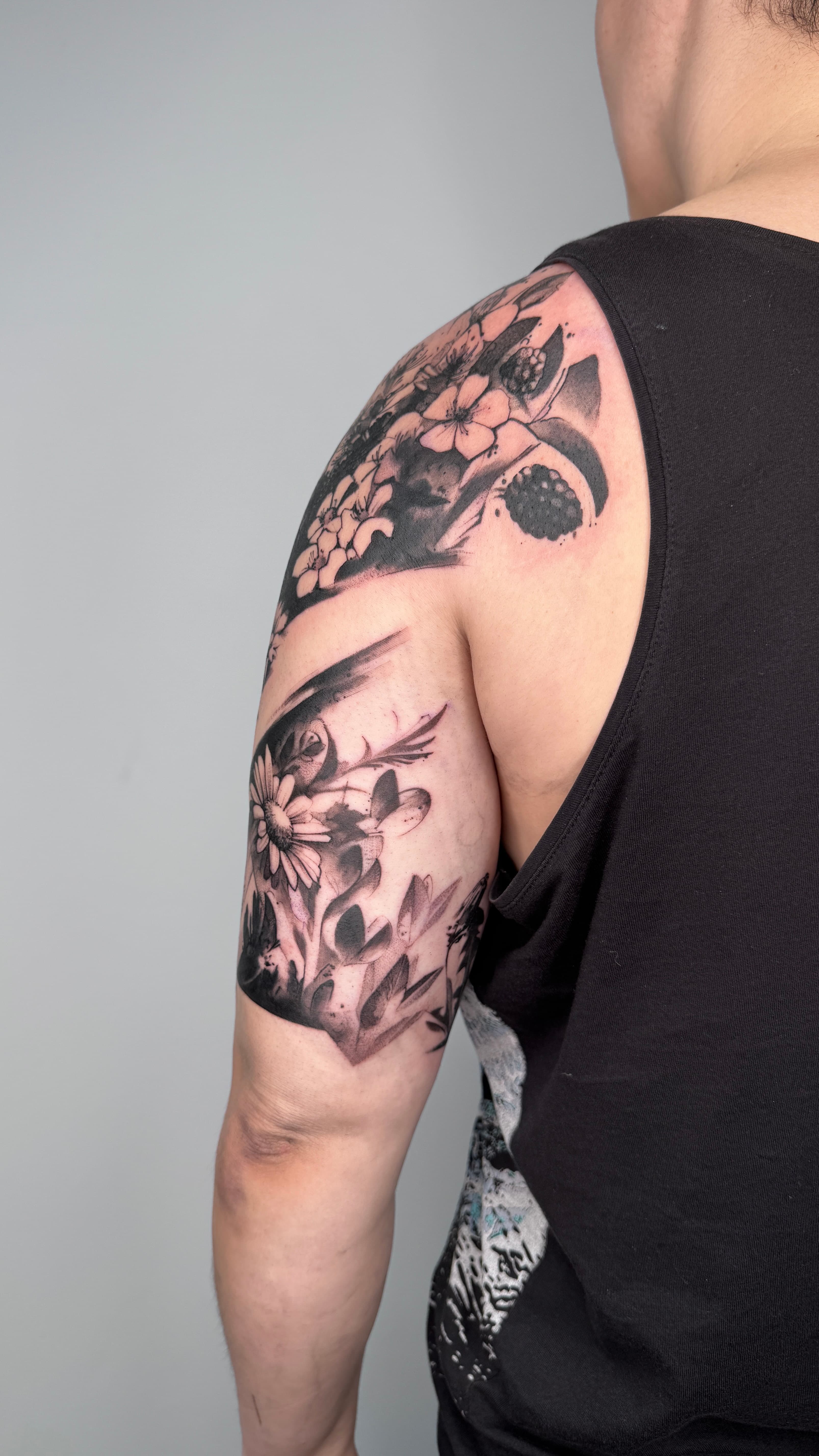 Detailaufnahme des abstrakten Blumenwiese Tattoos an der Schulter mit filigranen Linien und dunklen Akzenten