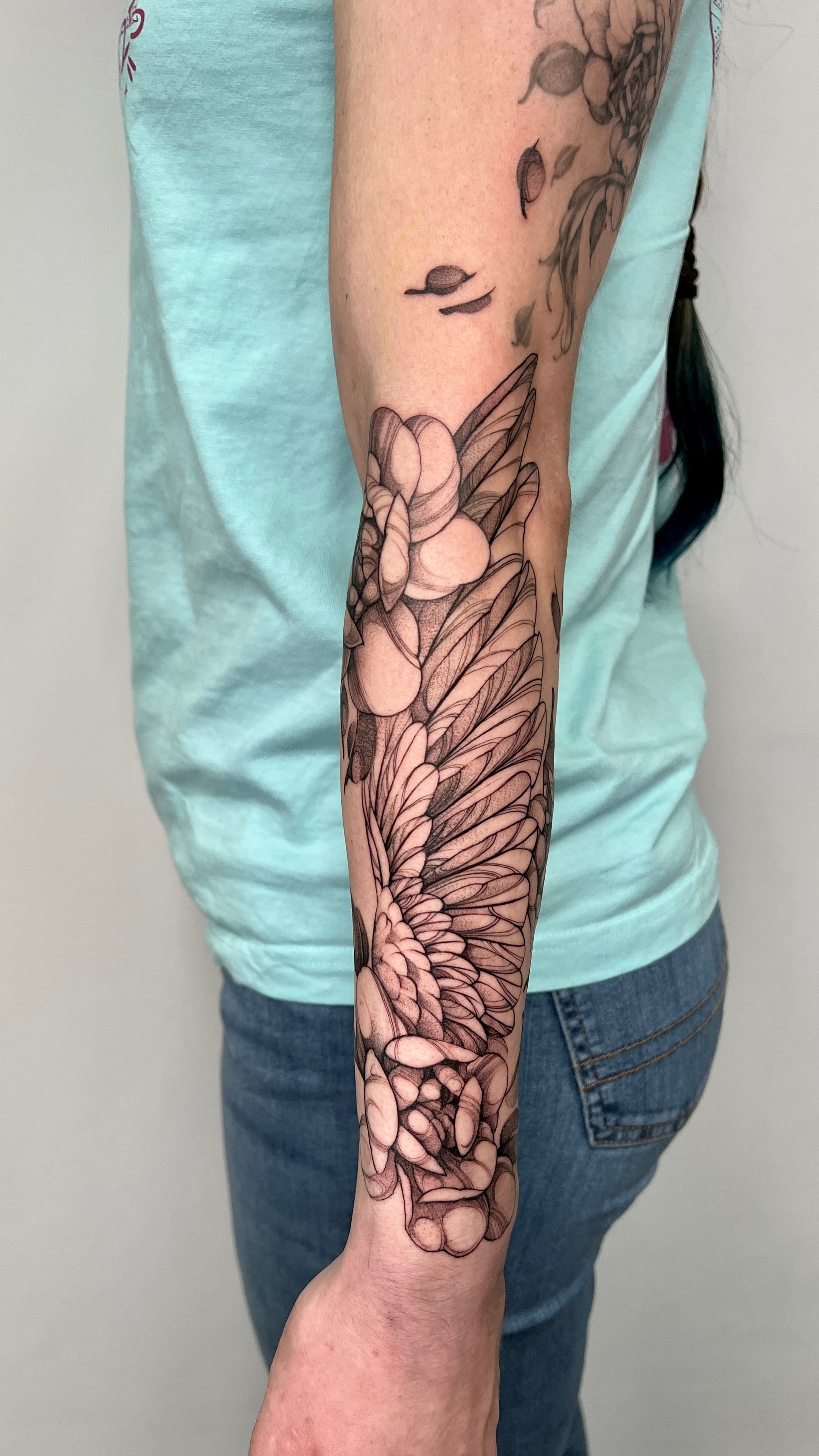 Tattoo von Lea Tattoo Artist in München - Fineline Flügel Tattoo mit floralen Element am Unterarm Fineline Flügel Tattoo mit Blumen am Unterarm, in München gestochen